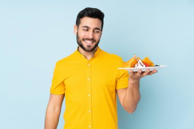 Mavi arka planda mutlu bir ifadeyle izole edilmiş waffle tutan beyaz bir adam.