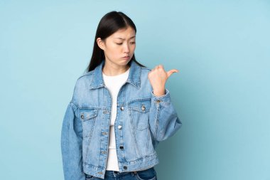 Arka planda izole edilmiş genç Asyalı kadın mutsuz ve bir tarafı işaret ediyor.