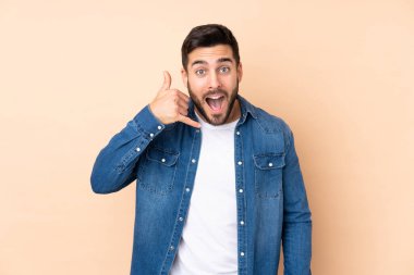 Beyaz tenli yakışıklı adam bej arka planda izole edilmiş, telefon jesti yapıyor. Bana geri dönüş işareti ver.