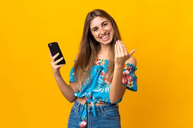 İzole edilmiş sarı arka planda cep telefonu kullanan genç bir kadın. Gelmene sevindim.