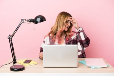 İşyerinde pembe arka planda dizüstü bilgisayarı olan genç bir bayan gülüyor.