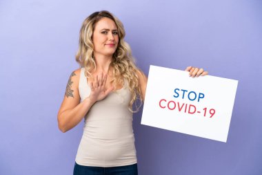 Mor arka planda izole edilmiş genç Brezilyalı bir kadın elinde yazılı bir levhayla Covid 19 'u durdur ve dur işareti yapıyor.