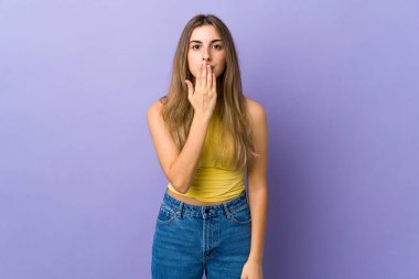 İzole edilmiş mor arka plan, ağzı elle kaplayan genç bir kadın.