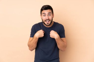 Beyaz tenli yakışıklı adam bej arka planda izole edilmiş ve yüzünde sürpriz bir ifade var.