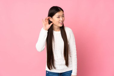 Asyalı genç bir kadın izole edilmiş arka planda bir şeyler dinlerken elini kulağına koyar.