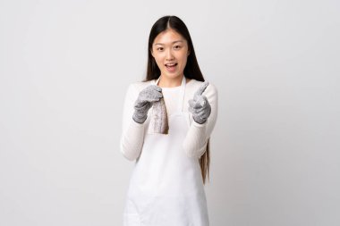 Önlük takan Çinli balıkçı, izole edilmiş beyaz arka planda çiğ balık tutuyor ve gülümsüyor.