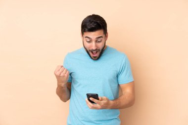 Beyaz tenli yakışıklı adam bej arka planda izole edilmiş, şaşırmış ve bir mesaj gönderiyor.