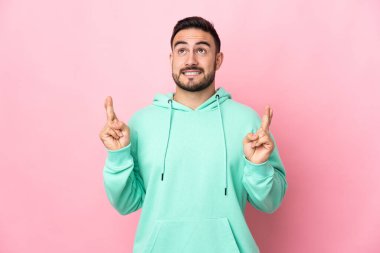 Beyaz tenli yakışıklı adam pembe arka planda izole edilmiş, parmaklarını çapraz yapıp en iyisini diliyor.