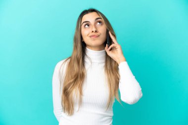 Mavi arka planda izole edilmiş cep telefonu kullanan beyaz bir kadın.