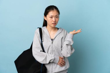 Spor çantalı genç Çinli kadın izole edilmiş mavi arka planda kuşkuları var.