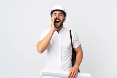 Miğferli ve elinde planları olan genç bir mimar beyaz arka planda izole edilmiş bağırıyor ve bir şey duyuruyor.