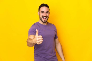 Beyaz tenli yakışıklı adam sarı arka planda izole edildi. Başparmakları havada, çünkü iyi bir şey oldu.