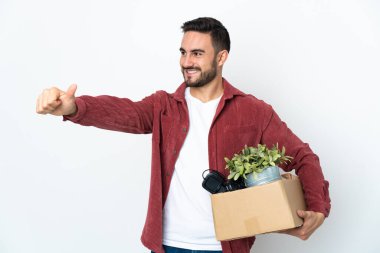 Beyaz arka planda izole edilmiş eşyalarla dolu bir kutuyu kaldırırken beyaz bir adam harekete geçiyor.