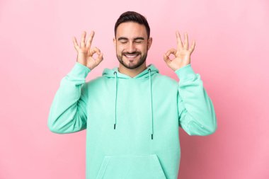 Zen pozisyonunda pembe arka planda izole edilmiş beyaz yakışıklı bir adam.