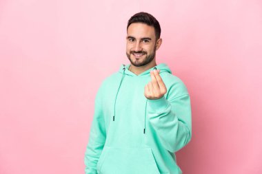 Beyaz tenli yakışıklı adam pembe arka planda izole edilmiş para hareketi yapıyor.