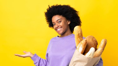 Genç Afrikalı Amerikalı bir kadın sarı arka planda izole edilmiş bir şey alıyor. Gülümserken bir fikir sunuyor.