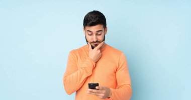 Kafkasyalı yakışıklı adam düşünüyor ve mavi arka planda bir mesaj gönderiyor.