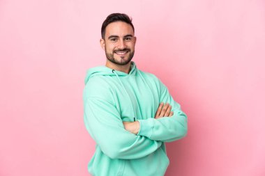 Pembe arka planda soyutlanmış, kolları bağlı ve ileriye bakan beyaz, yakışıklı genç bir adam.