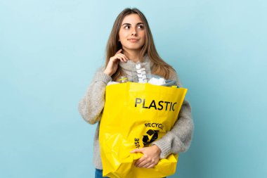 Bir çanta dolusu plastik şişeyi izole edilmiş mavinin üzerinde geri dönüştürmek için bir fikir tutarak.