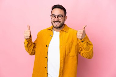 Pembe arka planda izole edilmiş beyaz, yakışıklı bir genç baş parmak hareketi yapıyor.