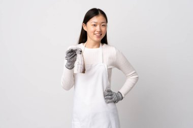 Çinli balıkçı önlük takıyor ve soyutlanmış beyaz arka planda çiğ balık tutuyor. Kolları kalçasında ve gülümsüyor.