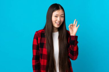 İzole edilmiş mavi arka planda genç bir Çinli kız parmaklarıyla işaret veriyor.