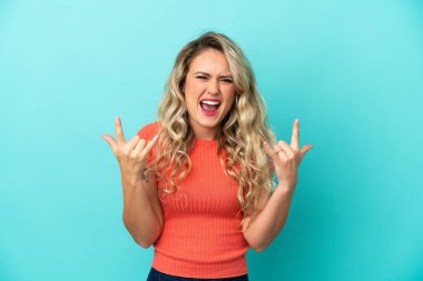 Mavi arka planda izole edilmiş genç Brezilyalı kadın boynuz hareketi yapıyor.