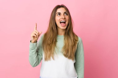 Soyutlanmış pembe arka planı olan genç bir kadın yukarı bakıyor ve şaşırıyor