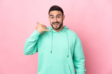 Pembe arka planda izole edilmiş beyaz, yakışıklı genç bir adam telefon jesti yapıyor. Bana geri dönüş işareti ver.