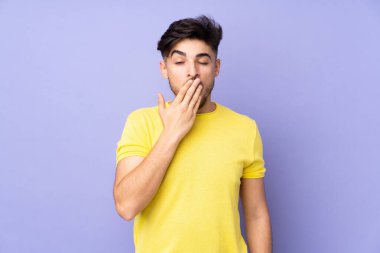 Arap yakışıklı adam izole edilmiş arka planda esniyor ve ağzını eliyle kapatıyor.