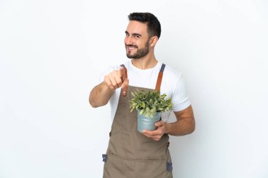 Bahçıvan elinde bir bitki tutuyor beyaz arka planda mutlu bir ifadeyle ön tarafı işaret ediyor.