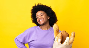 Genç Afrikalı Amerikalı bir kadın sarı arka planda izole edilmiş bir şey alıyor. Kolları kalçasında ve gülümsüyor.