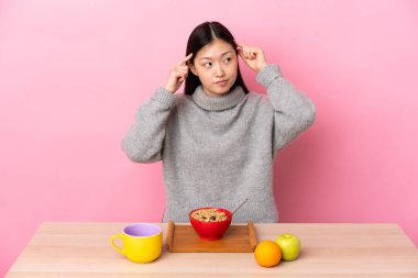 Genç Çinli kız bir masada kahvaltı yapıyor. Şüpheleri ve düşünceleri var.