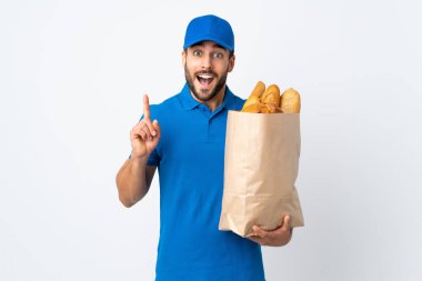 Bir çanta dolusu ekmek taşıyan teslimatçı beyaz arka planda izole edilmiş harika bir fikre işaret ediyor.