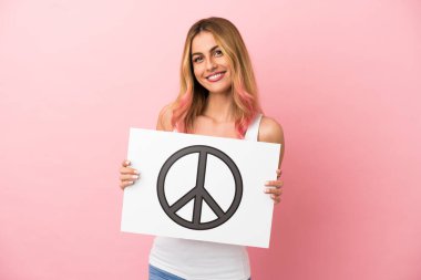 Soyutlanmış pembe arka planı olan genç bir kadın elinde mutlu bir ifadeyle barış sembolü olan bir pankart tutuyor.