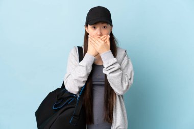 Spor çantalı genç Çinli kadın izole edilmiş mavi arka planda elleri ve ağzı kapalı.