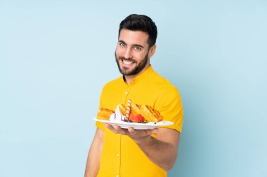 Mavi arka planda mutlu bir ifadeyle izole edilmiş waffle tutan beyaz bir adam.