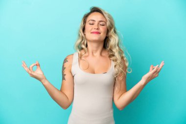 Genç Brezilyalı kadın Zen pozunda mavi arka planda izole edilmiş.