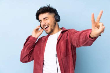 Arap yakışıklı adam mavi arka planda izole edilmiş müzik dinliyor ve şarkı söylüyor.