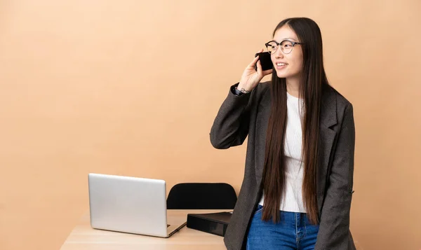 Chinese business woman in her workplace keeping a conversation with the mobile phone with someone