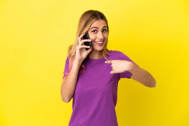 İzole edilmiş sarı arka planda cep telefonu kullanan genç bir kadın.