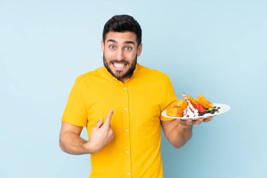 Mavi arka planda yüzü şaşırmış beyaz bir adam waffle tutuyor.