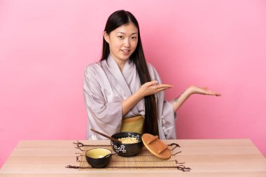 Kimono giyen genç Çinli kız ve erişte yiyor. Davet etmek için ellerini yana uzatıyor.