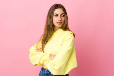 Soyutlanmış pembe arka planı olan genç bir kadın kollarını kavuşturuyor.