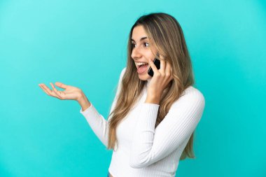 Mavi arka planda izole edilmiş cep telefonu kullanan genç, beyaz bir kadın.