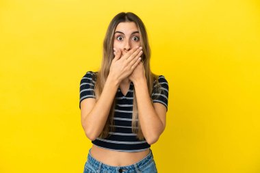 Sarı arka planda izole edilmiş genç beyaz kadın elleriyle ağzını kapatıyor.