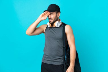 Spor çantalı genç adam mavi arka planda izole edilmiş, yorgun ve hasta bir yüz ifadesi var.