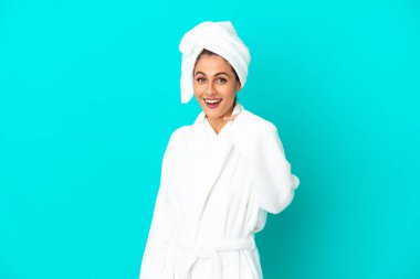 İzole edilmiş mavi arka planda bornozlu genç bir kadın. Sürpriz bir yüz ifadesi var.