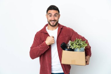 Beyaz arka planda izole edilmiş, sürpriz bir yüz ifadesi olan şeylerle dolu bir kutuyu alırken genç beyaz bir adam hamle yapıyor.