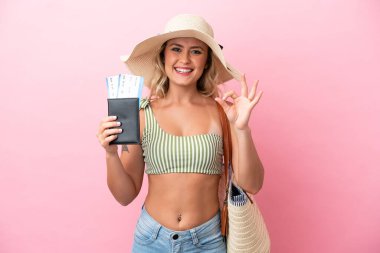 Yaz tatilinde mayo giyen genç Brezilyalı kadın pembe arka planda izole edilmiş, parmaklarıyla işaret veriyor.